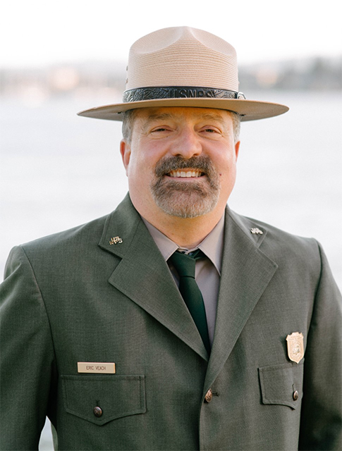 Eric Veach Portrait of a man in green and gray uniform and flathat from the chest up looking past the camera.