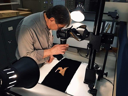 Seated man photographing an artifact on a black background with lights shining on the artifact