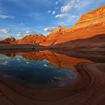 A reflecting pool of water in front of red cliffs at sunset.