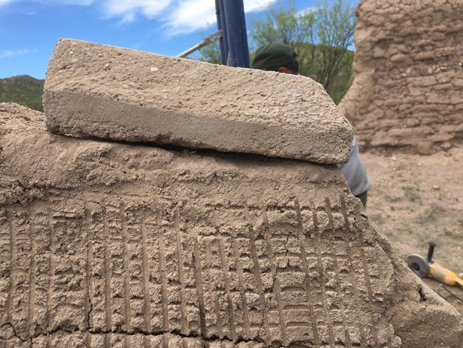 A adobe sits on top of a wall with cross hatching on it.