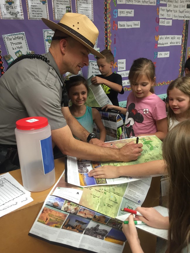 A man in ranger uniform with pen and maps, surrounded by students.