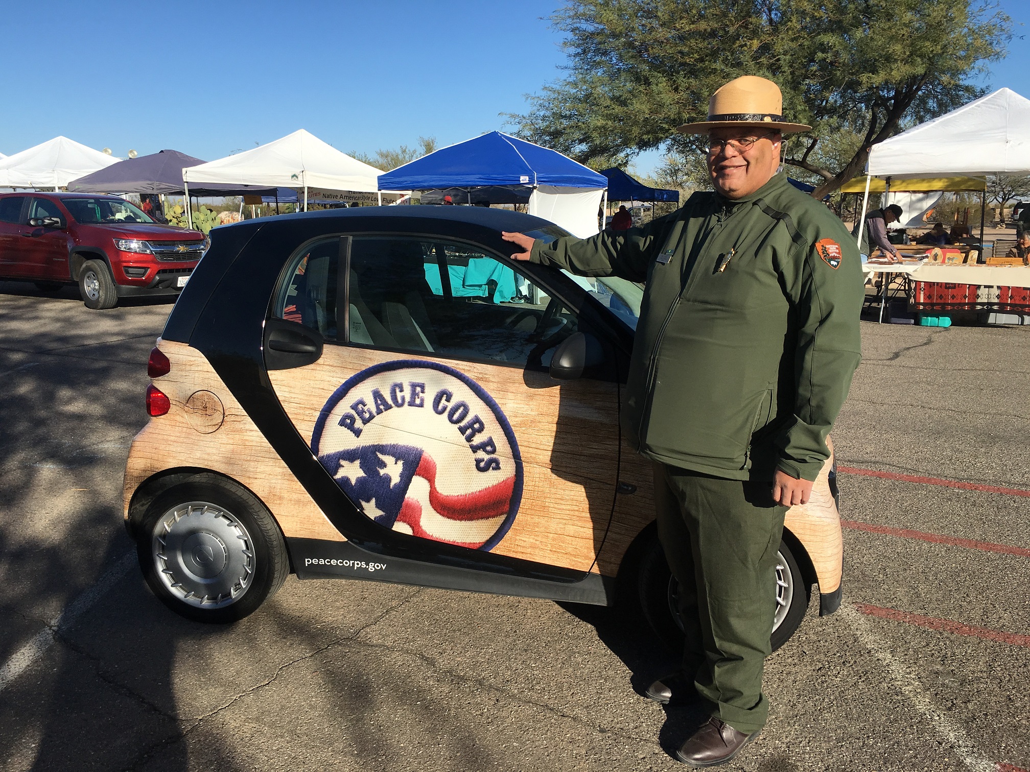 A man in green uniform and hat stands in front of a small electric car.