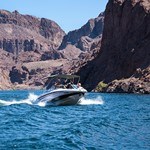 A speed boat in blue water with tall cliffs.