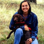 Sierra Lohr A smiling woman with long hair and glasses holding a brown dog with a red collar.