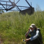 A woman sitting on a stream bank with bridge behind.