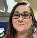 A woman in glasses looks at the camera