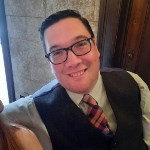 A smiling man in glasses leans back to look at a camera. A smiling man in glasses leans back to look at a camera.