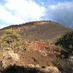 A mostly black cinder cone with cloudy sky.