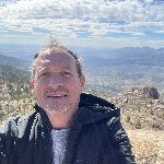 A smiling man standing in front of a mountain range.