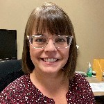 White_150 Headshot of a woman with bangs and glasses smiles directly into the camera.