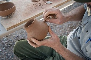 Hands around a clay pot that looks still damp.