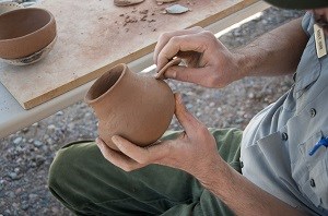 TONT Pottery Demo Hands around a clay pot that looks still damp.