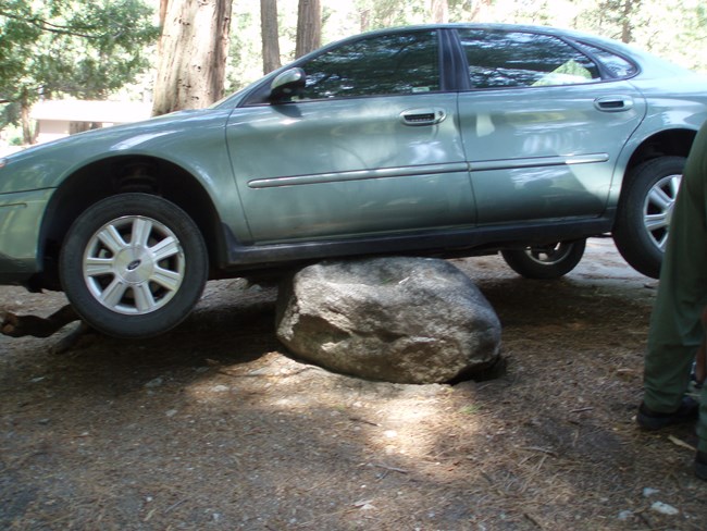 A car is balanced on a rock in a developed area.