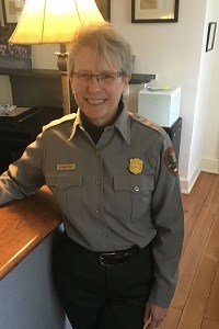 Deanna Ochs a woman in a park ranger uniform poses in front of a lamp and desk