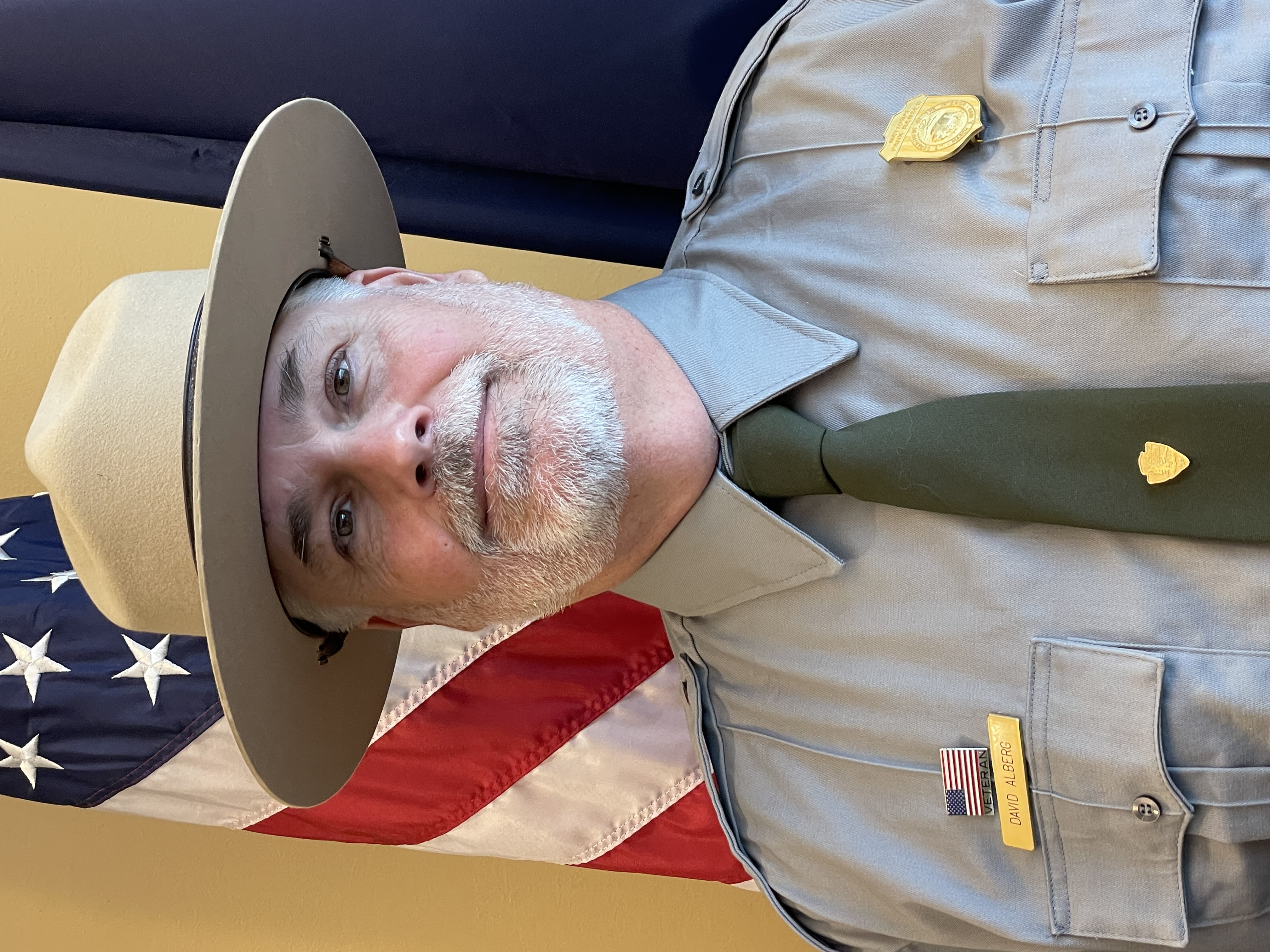 Dave Alberg Man in a NPS uniform beside an American flag