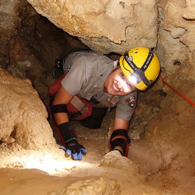 A female ranger crawling through a small passage in a cave.