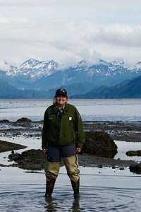 Kara Lewandowski a park ranger stands in tidal water in waders with mountains in the background