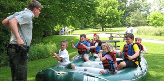Adult ranger giving a group of kids instruction on land in a raft.
