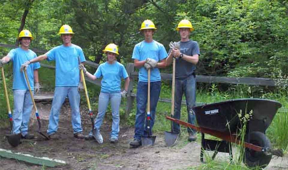 five workers wearing hardhats standing next to a wheelbarrow five workers wearing hardhats standing next to a wheelbarrow