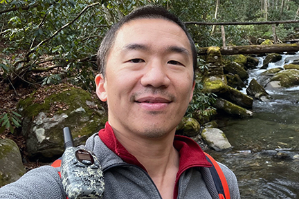 ShihMing Huang ShiMing Huang stands with a backdrop of a rushing stream and rustic trail bridge.