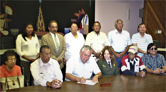 Tribal Consultation at Sand Creek Massacre NHS A group of people stand or sit around a table where a man signs a document.