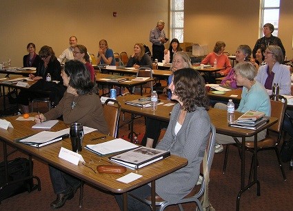 People sitting at several rows of tables with notebooks and papers.