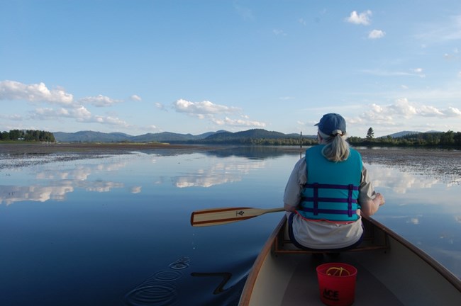 paddler with back to us sitting in bow looking over serene water setting