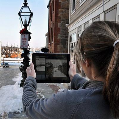 Woman holds up tablet with tour of downtown harbor walking tour