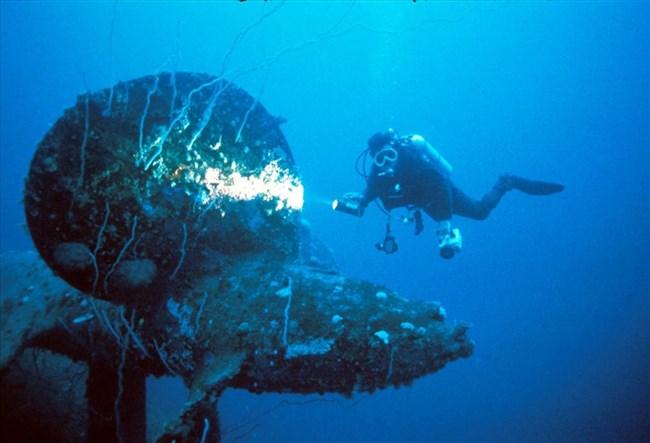 Diver shines flashlight at wreck underwater