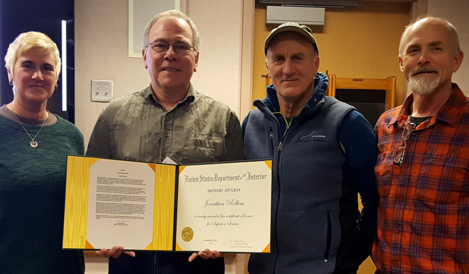 Jon Rollens hold as superior service award. He is flanked by three other people.