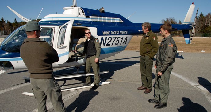 Three men stand and listen to a man pointing at something in a helicopter.
