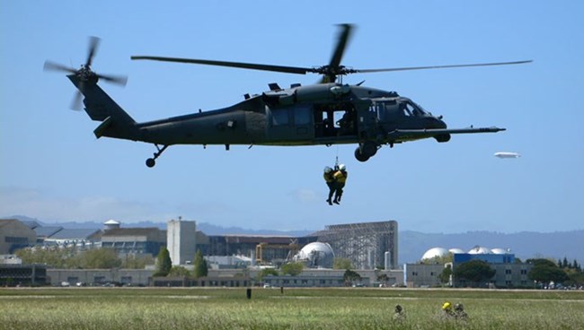 Hoist training Two people hang from a hoist line below a large hovering helicopter.