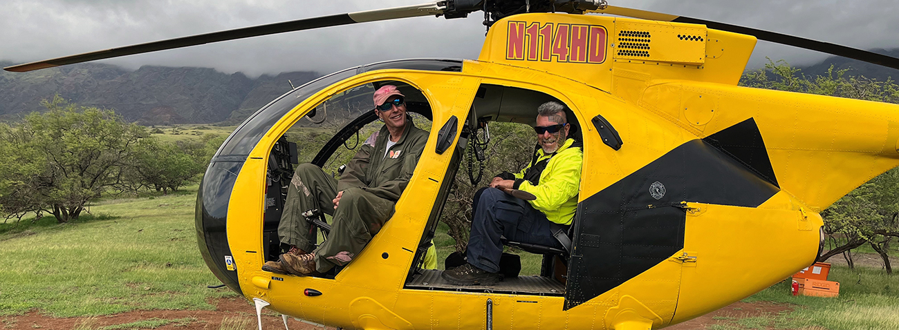 Timmy Bailey (right) A pilot sits in the front of a yellow helicopter while a man in personal protective equipment sits in back.