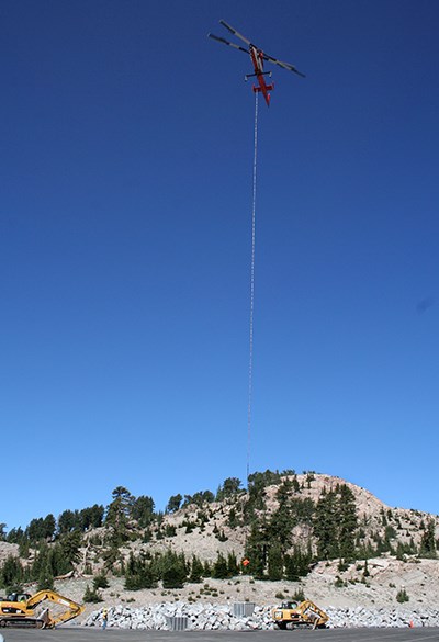 A helicopter lifts a slingload from a pile of rocks.
