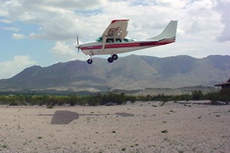 lt= A patrol plane flies in for a landing in scrubby desert landscape.