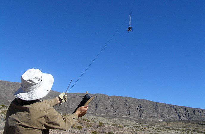 A person uses a gloved hand to fly a kite with a digital camera attached