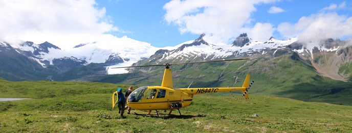 A person carries the door of a helicopter near a helicopter on tundra with mountain backdrop.
