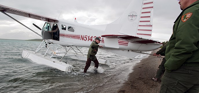 A man in NPS uniform wades from a floatplane to shore