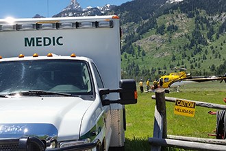 lt= An ambulance waits at the entrance to a helibase while crew members unload a patient from a helicopter.