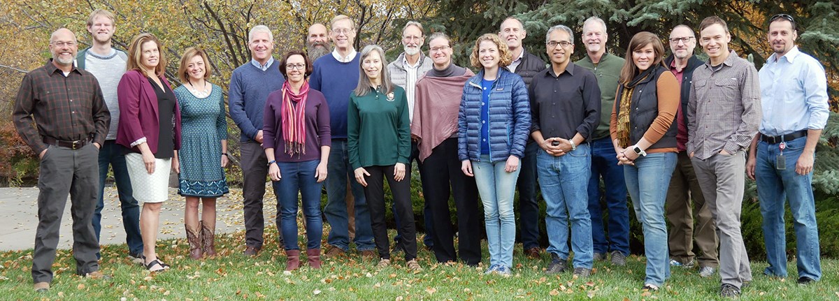 CCRP staff photo (2019) About twenty people standing in grass clearing with trees in background