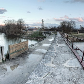 ServiceAreaImage_08 An abandoned bridge crosses over a river under a cloudy grey sky.