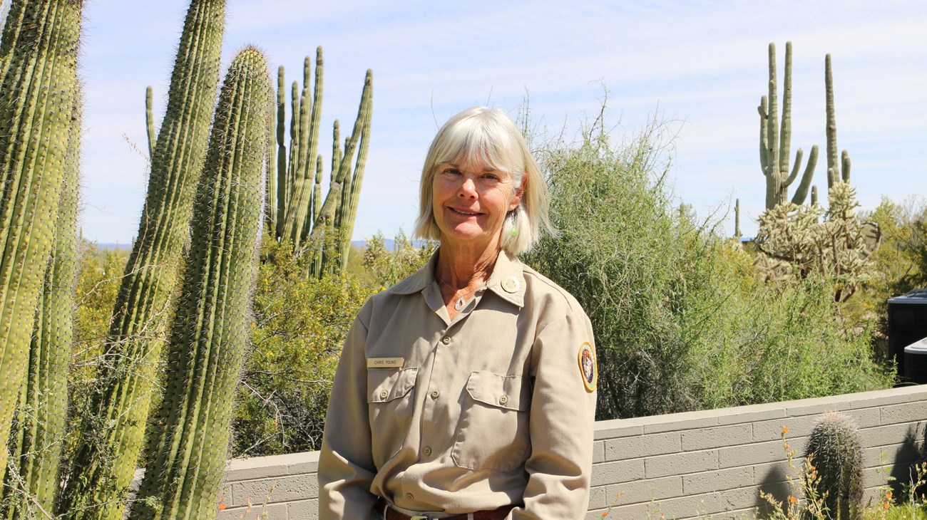 A woman volunteer stands smiling in front of an organ pipe cactus.