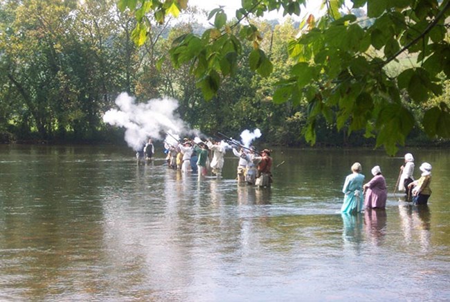 People in period costume firing muskets while standing in the Watauga River