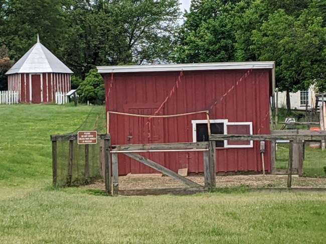 Red wooden building with tin roof with a fenced area in front of the doors