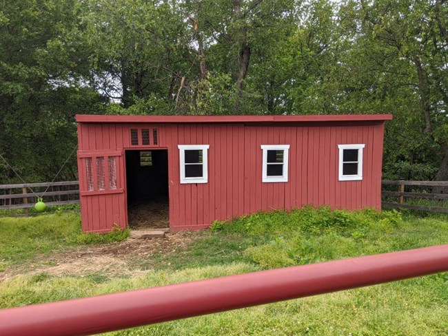 Red wood building with door on the left with three windows on the right.