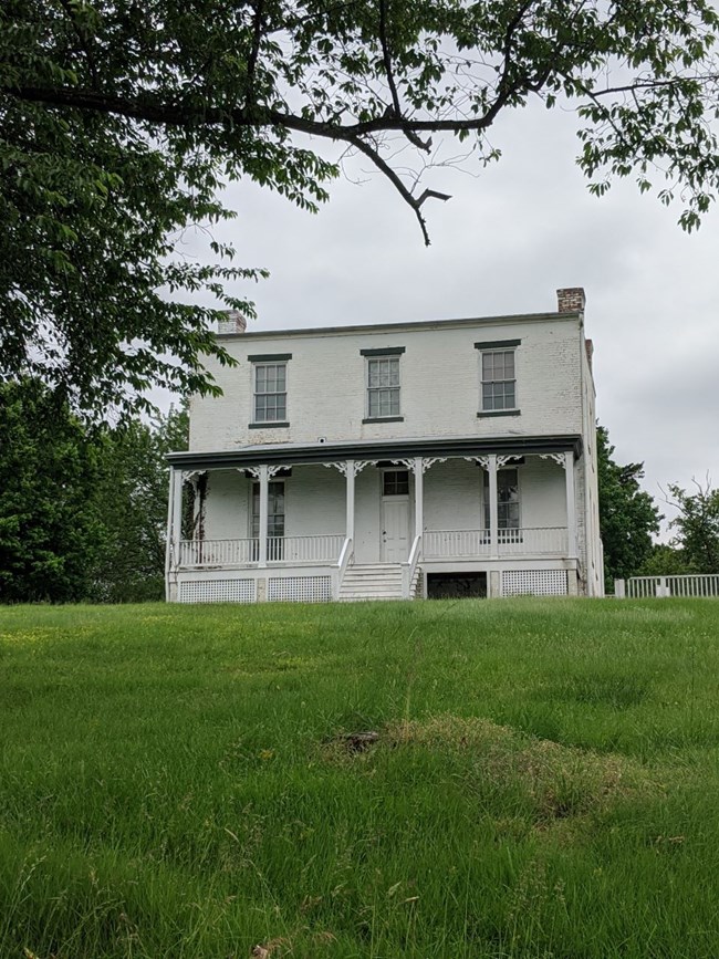 White two-story brick house with porch sitting atop a grassy hill