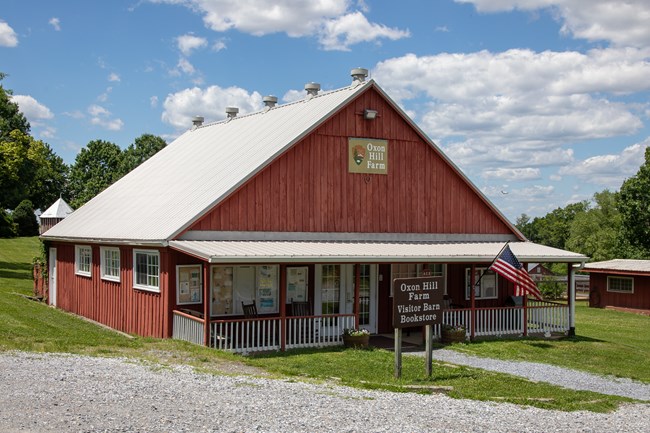 A red barn with a porch surrounded by grass and a gravel path.