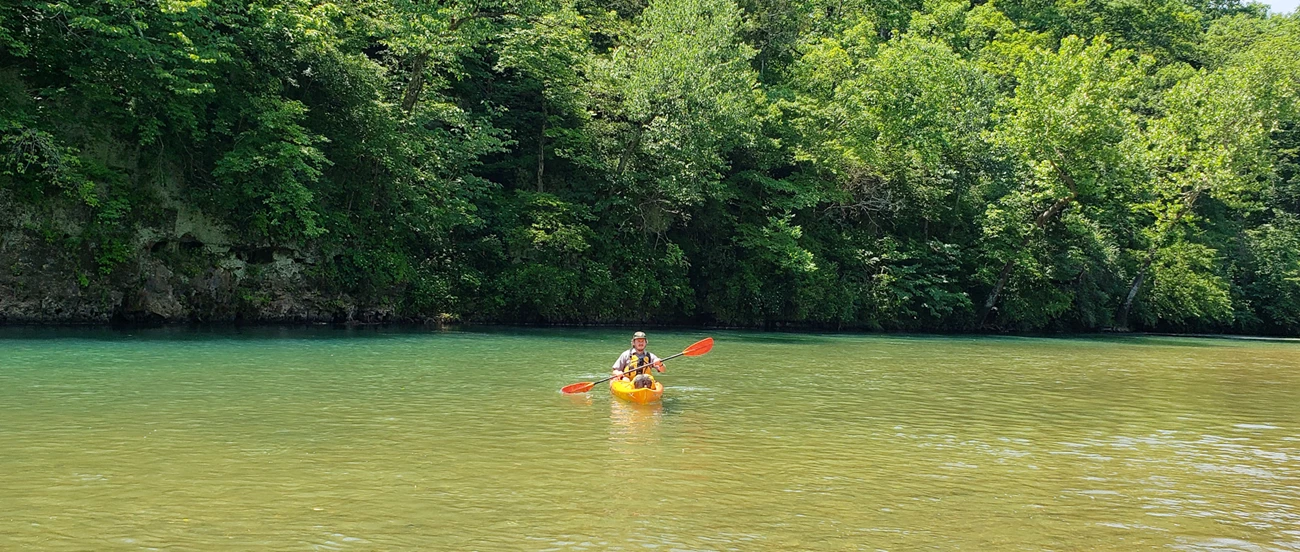 A park ranger floating near Current River State Park. A park ranger floats in an orange kayak. The river is calm and blue.