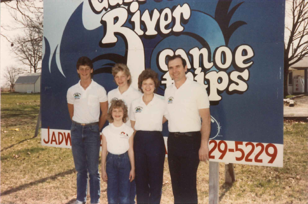 Darrel Blackwell and Family - (front) Amanda, (back; left to right) Brad, Scott, Shelia, and Darrell Blackwell From the 70s or 80s: A family of 5 stands before a small billboard. There is a mother, a father, 2 older sons, and a younger daughter. They all smile brightly at the camera, and they all wear white polo shirts. The sign is a billboard for the Jadwin Canoe