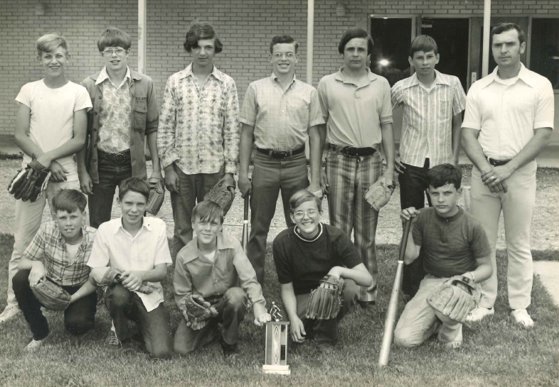 Darrel Blackwell (far right) with the Oak Hill R-1 baseball team From the 70s or 80s: A group of teenage baseball players pose with their coach. Half kneel in the grass, while the other half stand behind. There is a trophy in front of the team, and various members hold bats and gloves.